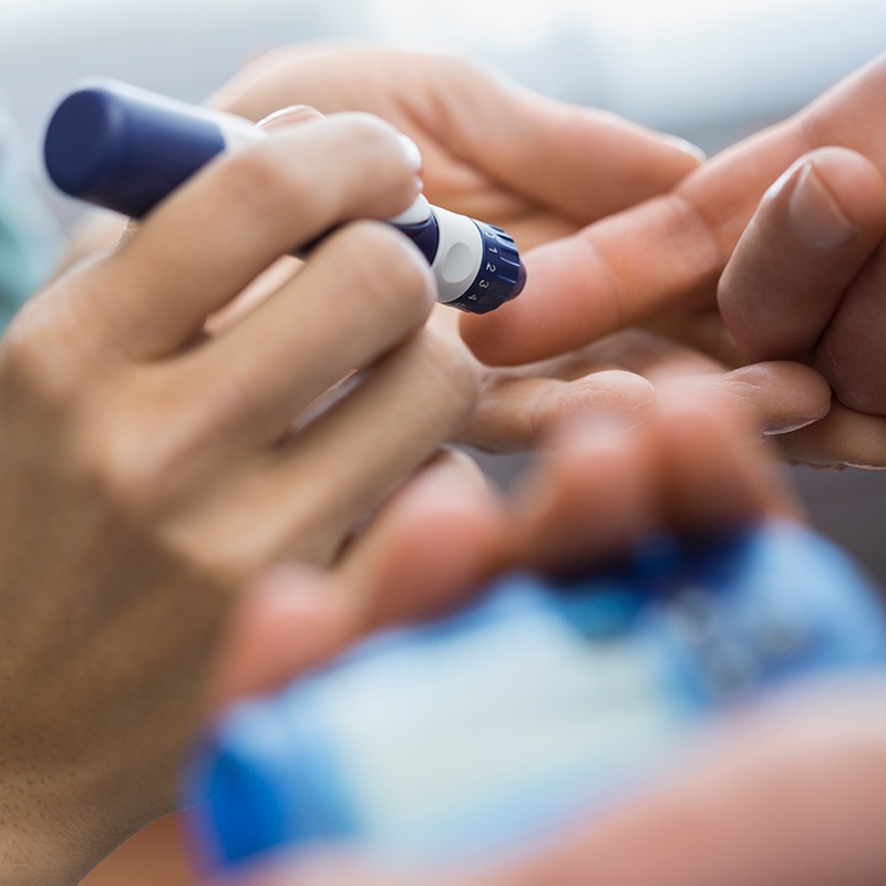A healthcare practitioner administers an injection to a patient's finger with an insulin pen