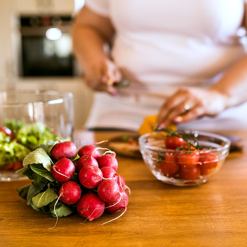 Radishes and a bowl strawberries sit on a counter while a woman prepares a healthy meal